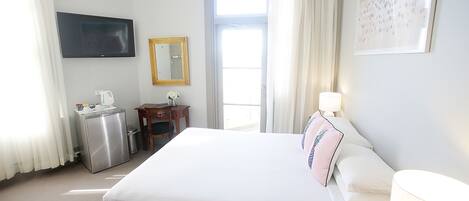 Una habitación de hotel con cama, escritorio, silla, televisor, ventana y puerta.