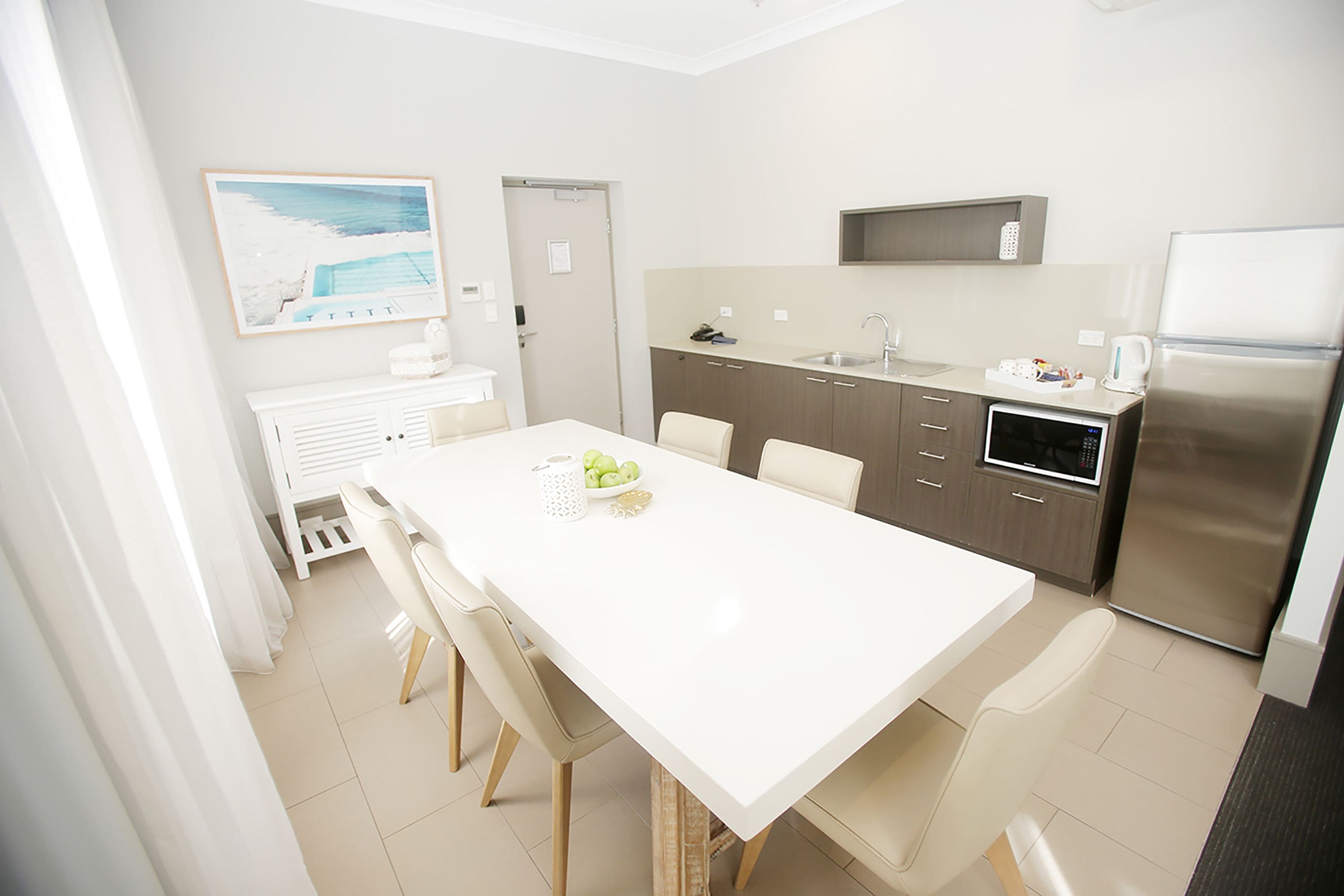 A modern kitchen with a white countertop, stainless steel appliances, and a dining area with a white table and chairs.