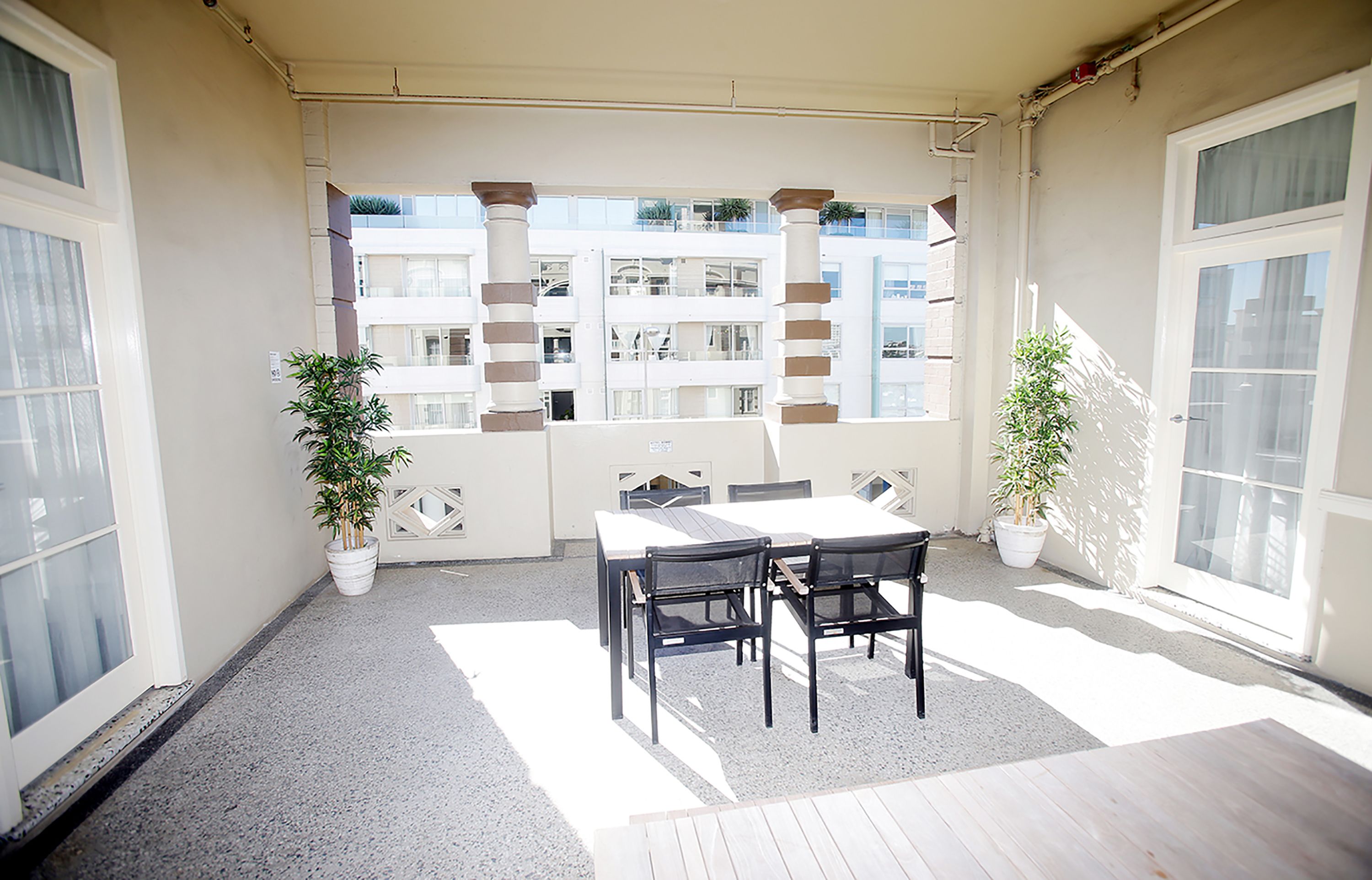 A balcony with a table and chairs, potted plants, and a view of a building with balconies.