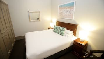 A neatly made bed with a wooden headboard, two bedside lamps, a framed mirror, and a beach-themed wall art.