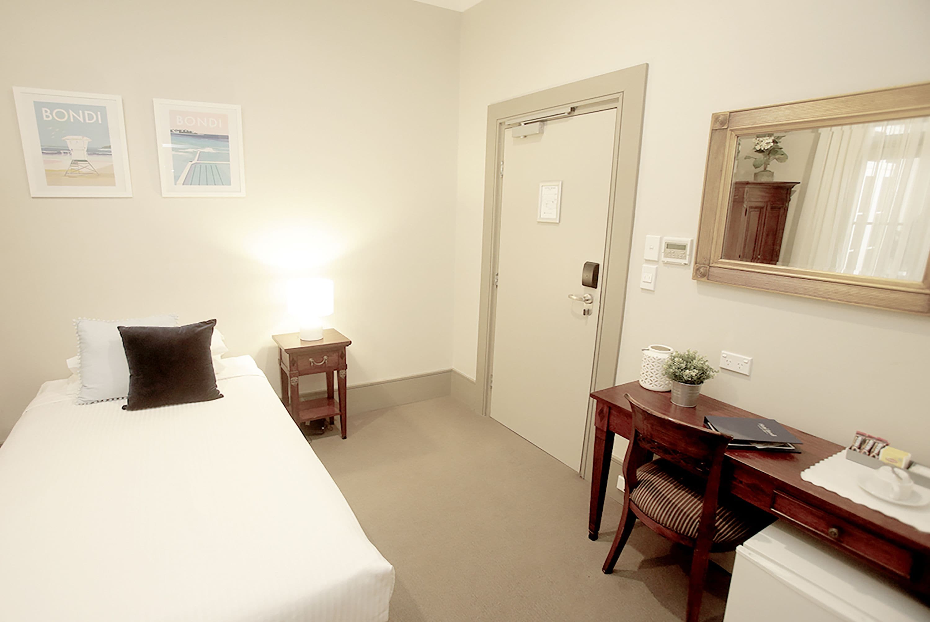 A hotel room with a bed, a desk, a chair, a mirror, and two framed pictures on the wall.