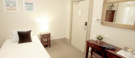 A hotel room with a bed, a desk, a chair, a mirror, and two framed pictures on the wall.