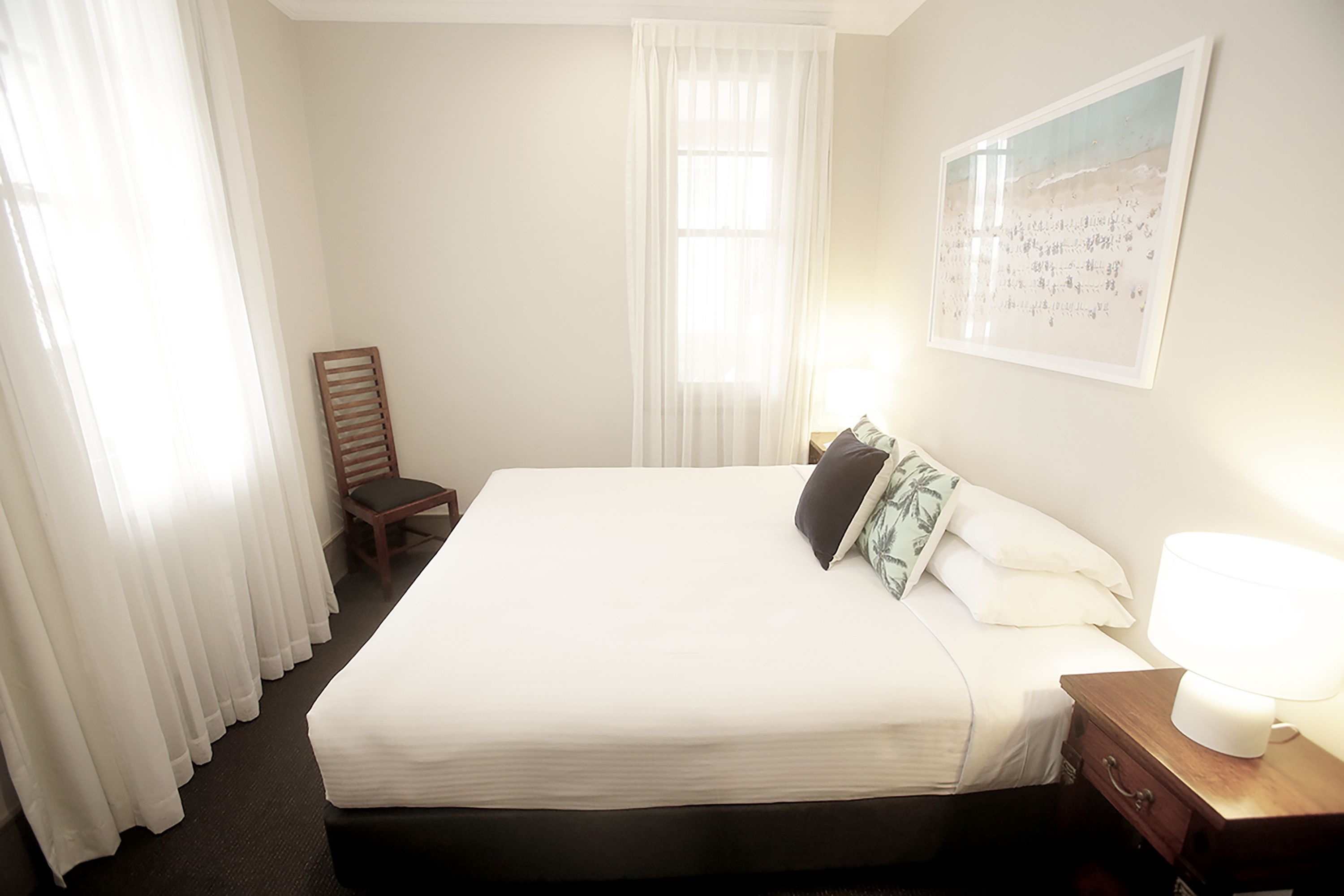 A hotel room with a large bed, a nightstand with a lamp, a chair, and a painting on the wall.