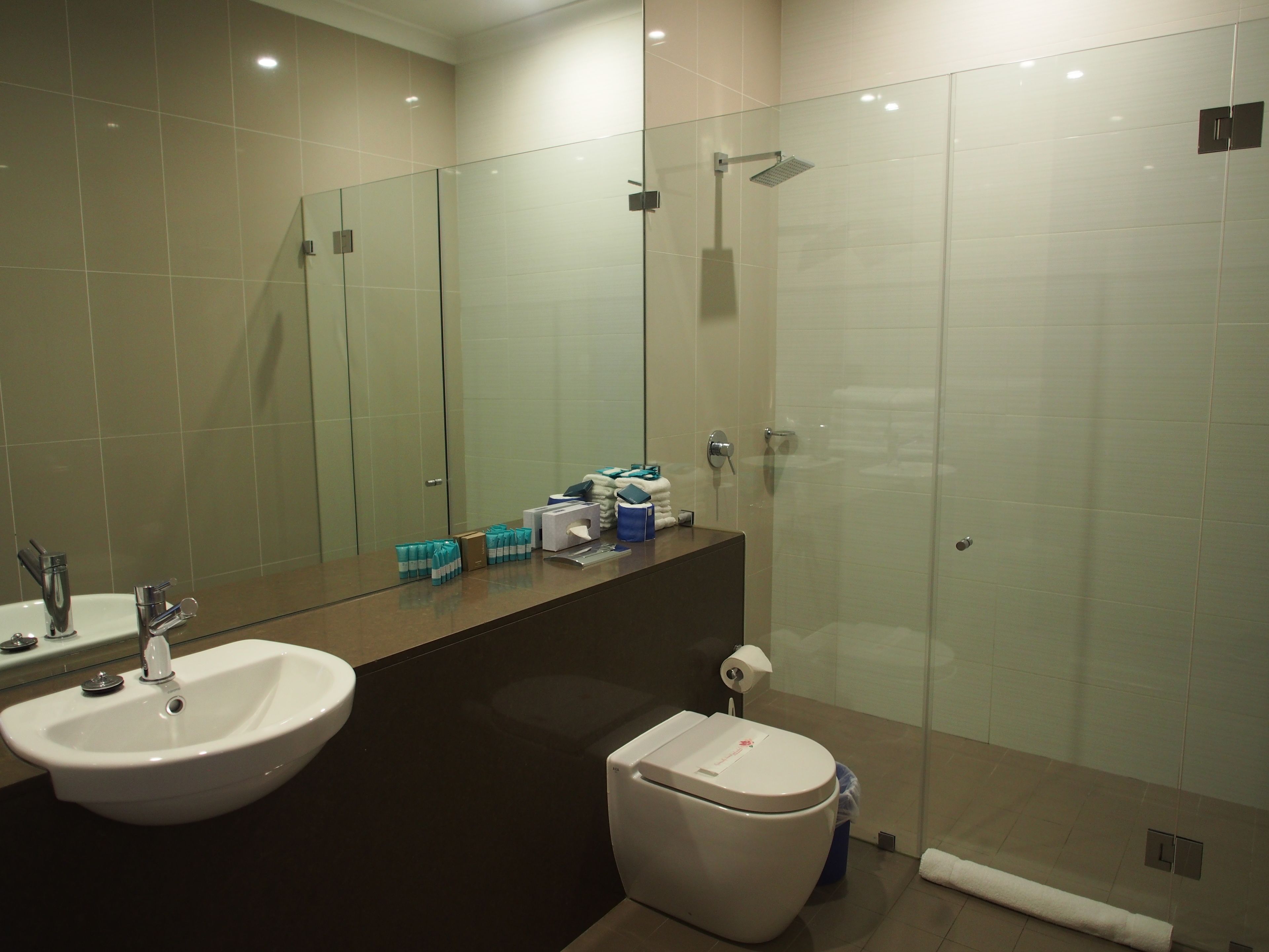 A modern bathroom with a large mirror, a sink, a toilet, and a shower area.
