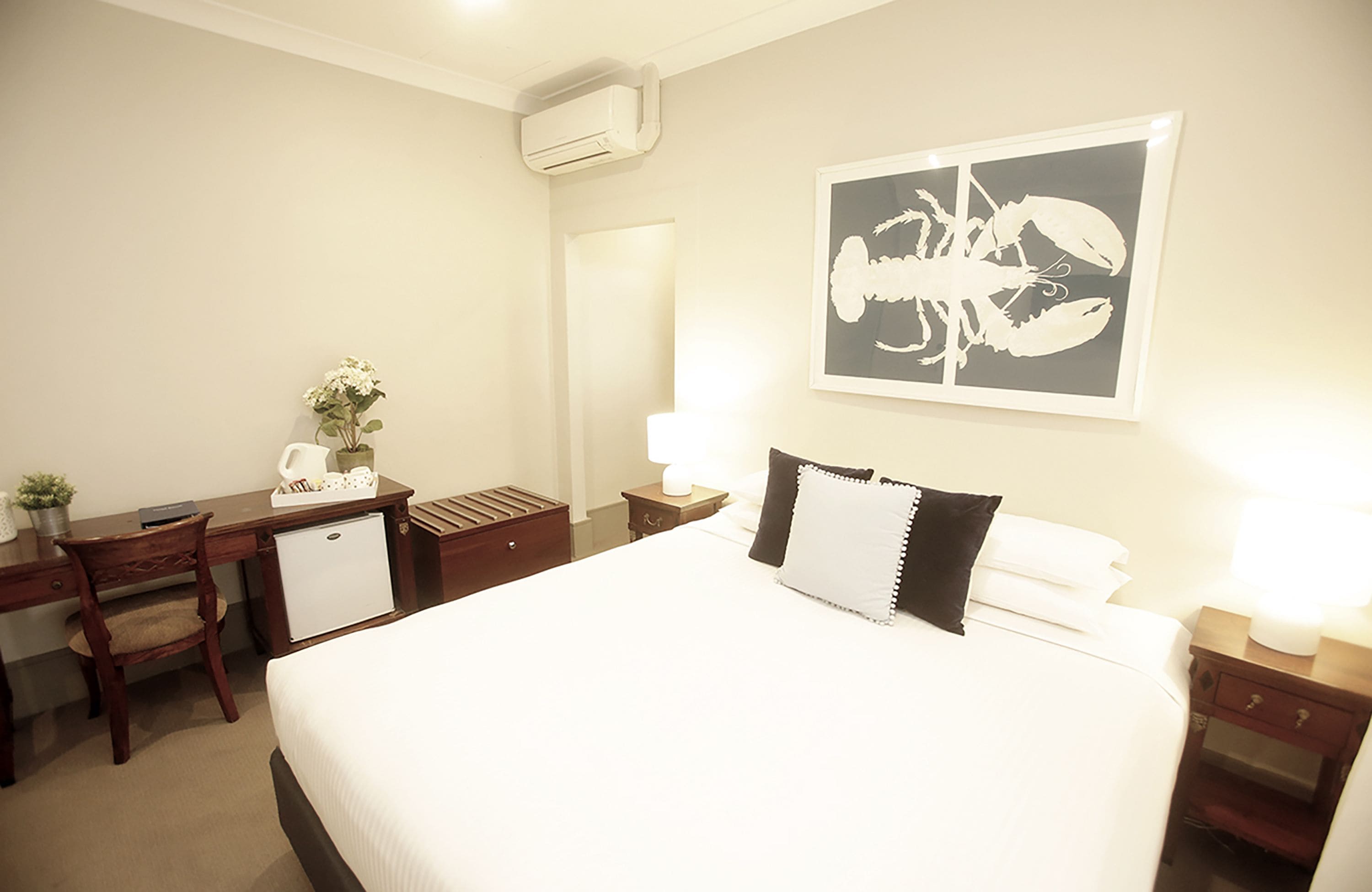 A hotel room with a bed, desk, chair, and a wall-mounted air conditioner.