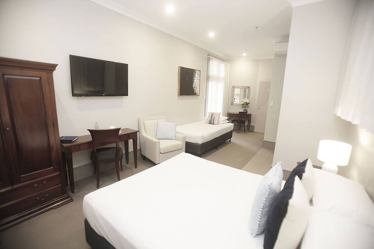 A hotel room with a bed, a desk, a chair, a wardrobe, a television, and a bathroom.