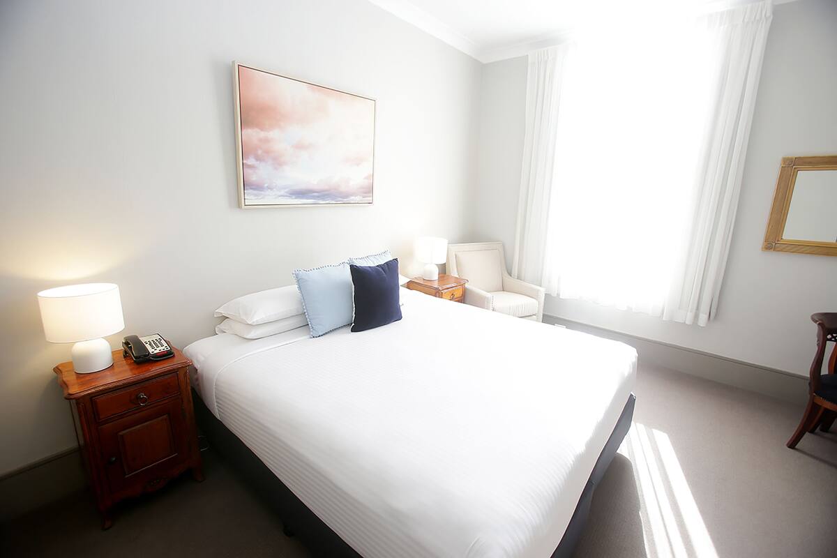 A hotel room with a neatly made bed, a bedside table with a lamp, a telephone, and a chair.