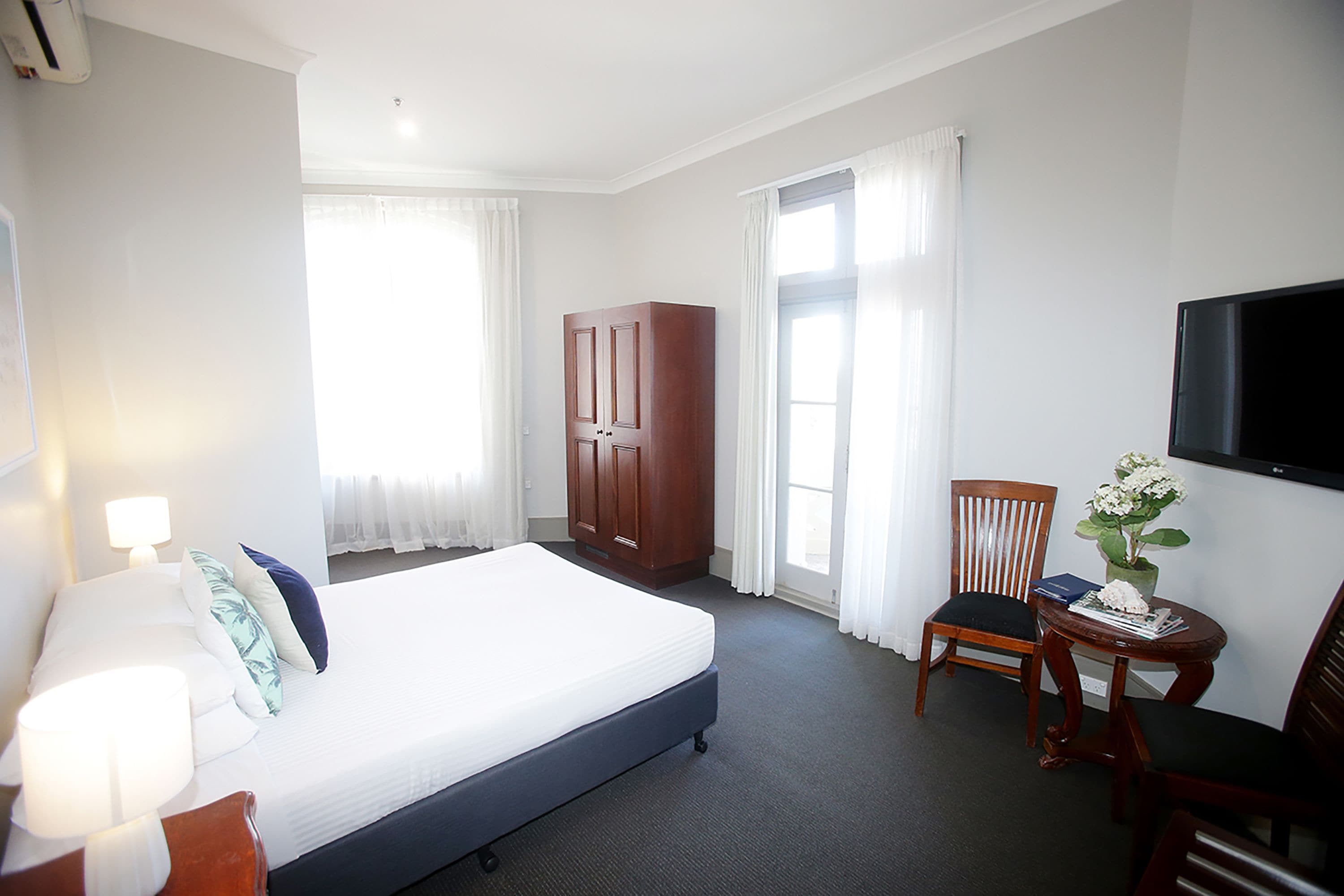 A hotel room with a bed, a desk, a chair, a wardrobe, and a TV.