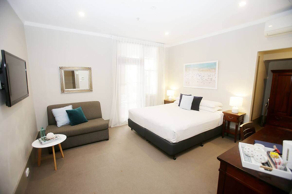 A hotel room with a bed, a sofa, a small table, a TV, and a desk with a chair.