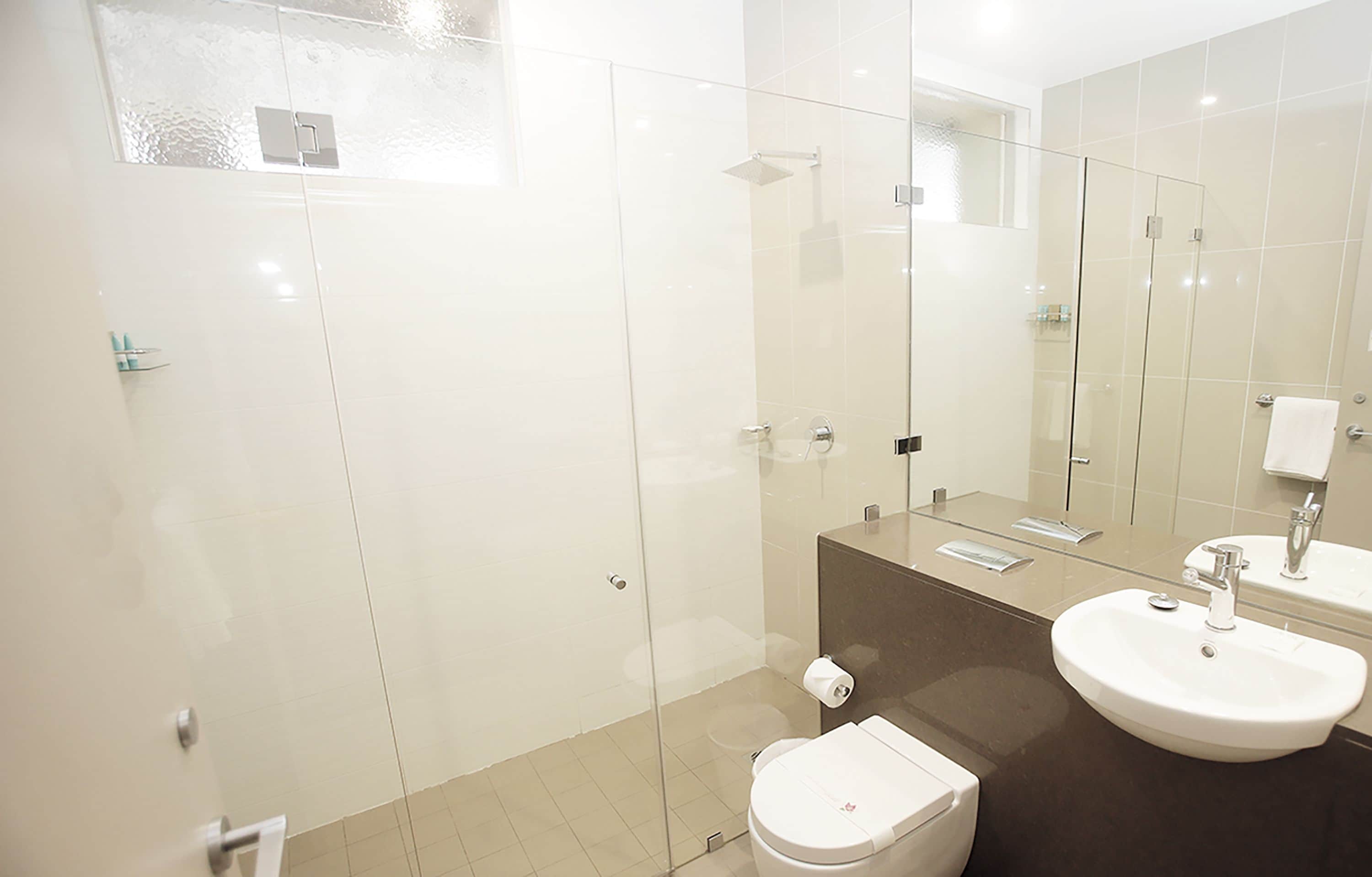 A modern bathroom with a glass-enclosed shower, a white toilet, and a large sink with a mirror above it.