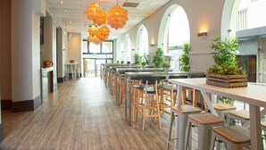 A spacious indoor area with long tables and chairs, arched windows, and hanging orange lamps. - Hotel Bondi (Bondi Beach)