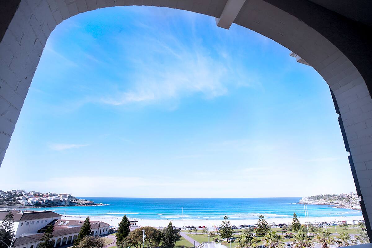 A view through an arched window of a coastal area with a beach, ocean, and buildings in the distance.