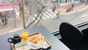 A breakfast tray with toast, a mug of coffee, and a glass of orange juice on a table by a window. - Philstay Ehwa Boutique (Seoul)