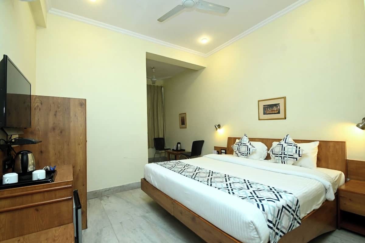 A hotel room with a bed, bedside table, lamp, and a television on a wooden cabinet.