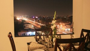 A dining table set with plates, cutlery, and a vase with a single flower, overlooking a cityscape at night with illuminated streets and buildings. - Hotel Yulia (Jaipur)