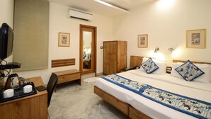 A hotel room with a bed, bedside table, chair, desk, and wardrobe. - Hotel Yulia (Jaipur)