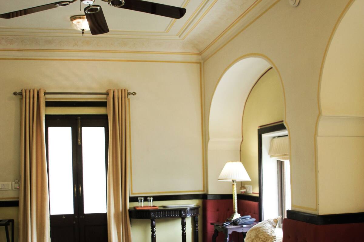 Hotelkamer met twee bedden, een plafondventilator, een bureau met lamp en uitzicht buiten via een deur.