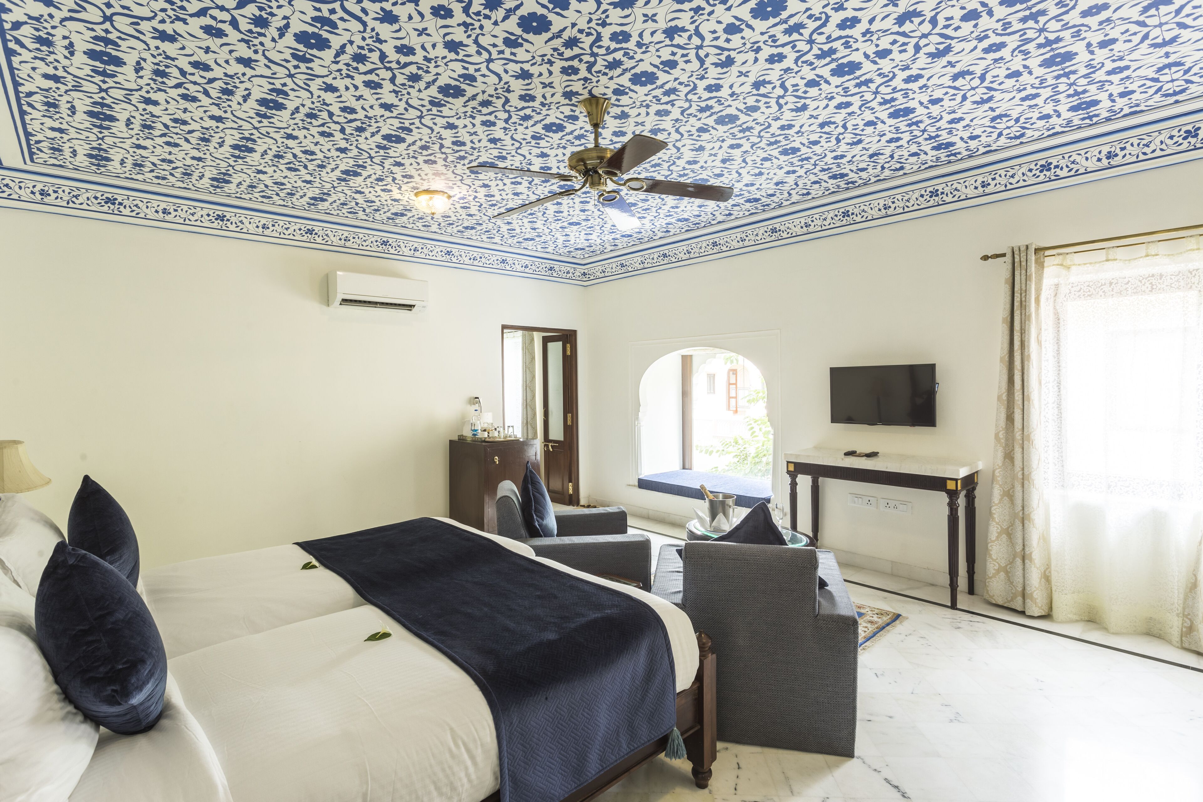 A hotel room with a bed, a desk, a chair, a TV, and a ceiling fan.