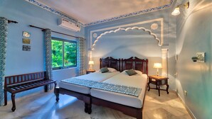 Un dormitorio con una cama grande, dos mesitas de noche, un banco y una ventana con vistas a zonas verdes.