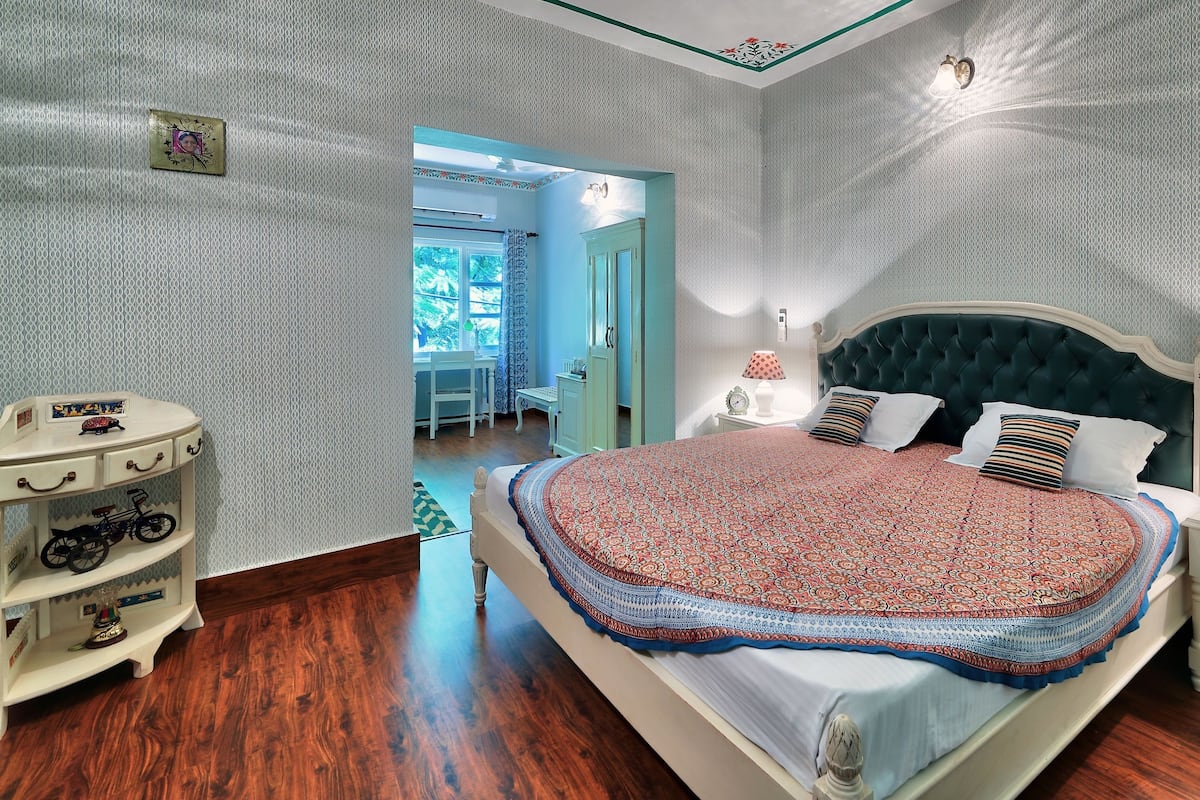 Une chambre à coucher avec un grand lit, une table de chevet, une commode et une porte donnant sur une autre pièce.