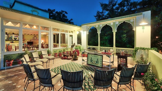 Un patio exterior bien iluminado con comedor, sillas y una mesa.