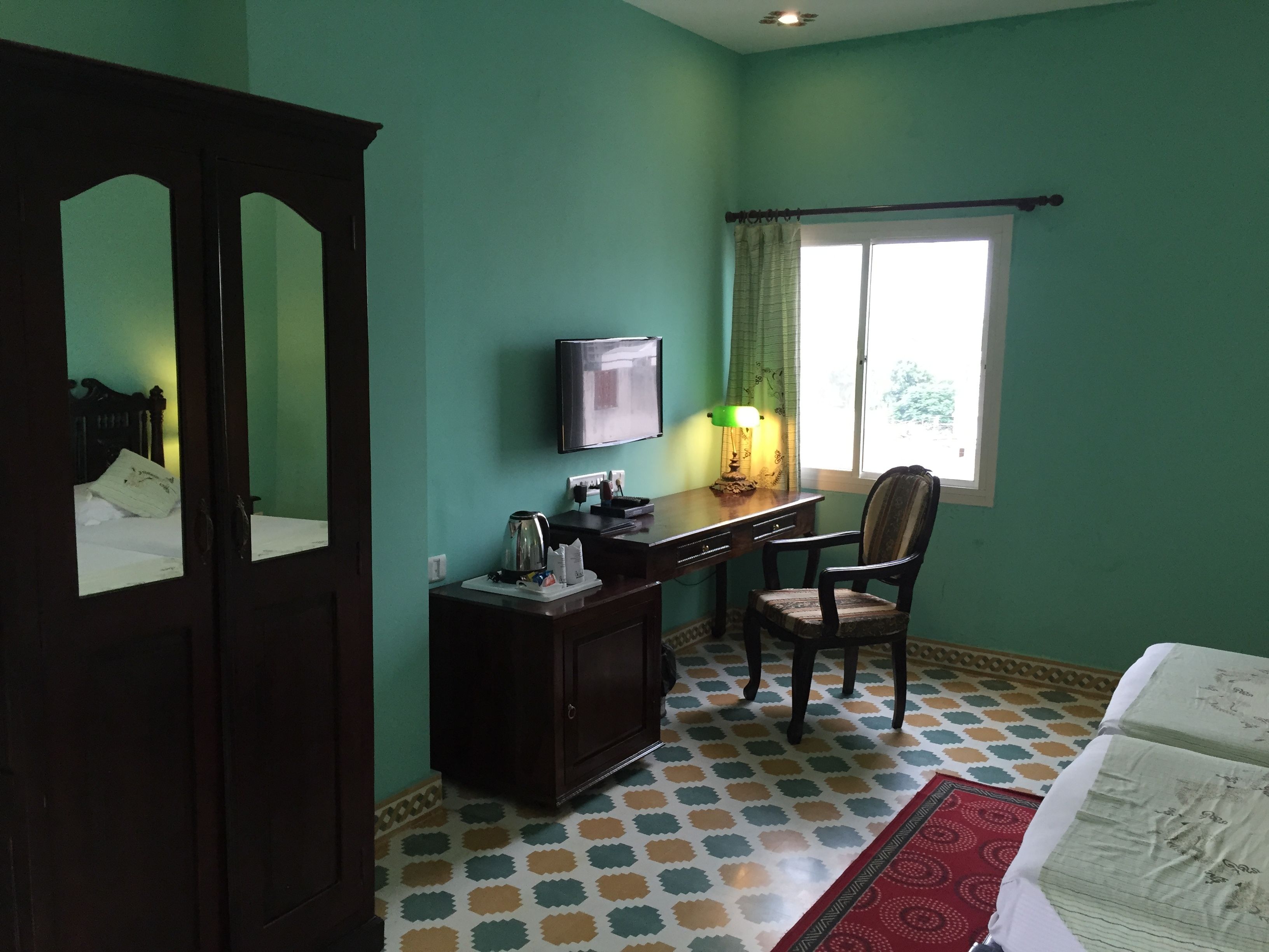 Une chambre d’hôtel avec une armoire en bois, un bureau avec une télévision, une chaise et une fenêtre avec des rideaux.