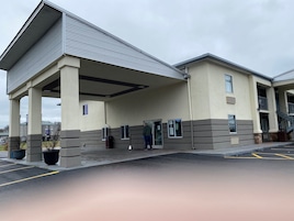 A building with a covered entrance, a staircase, and a parking lot.