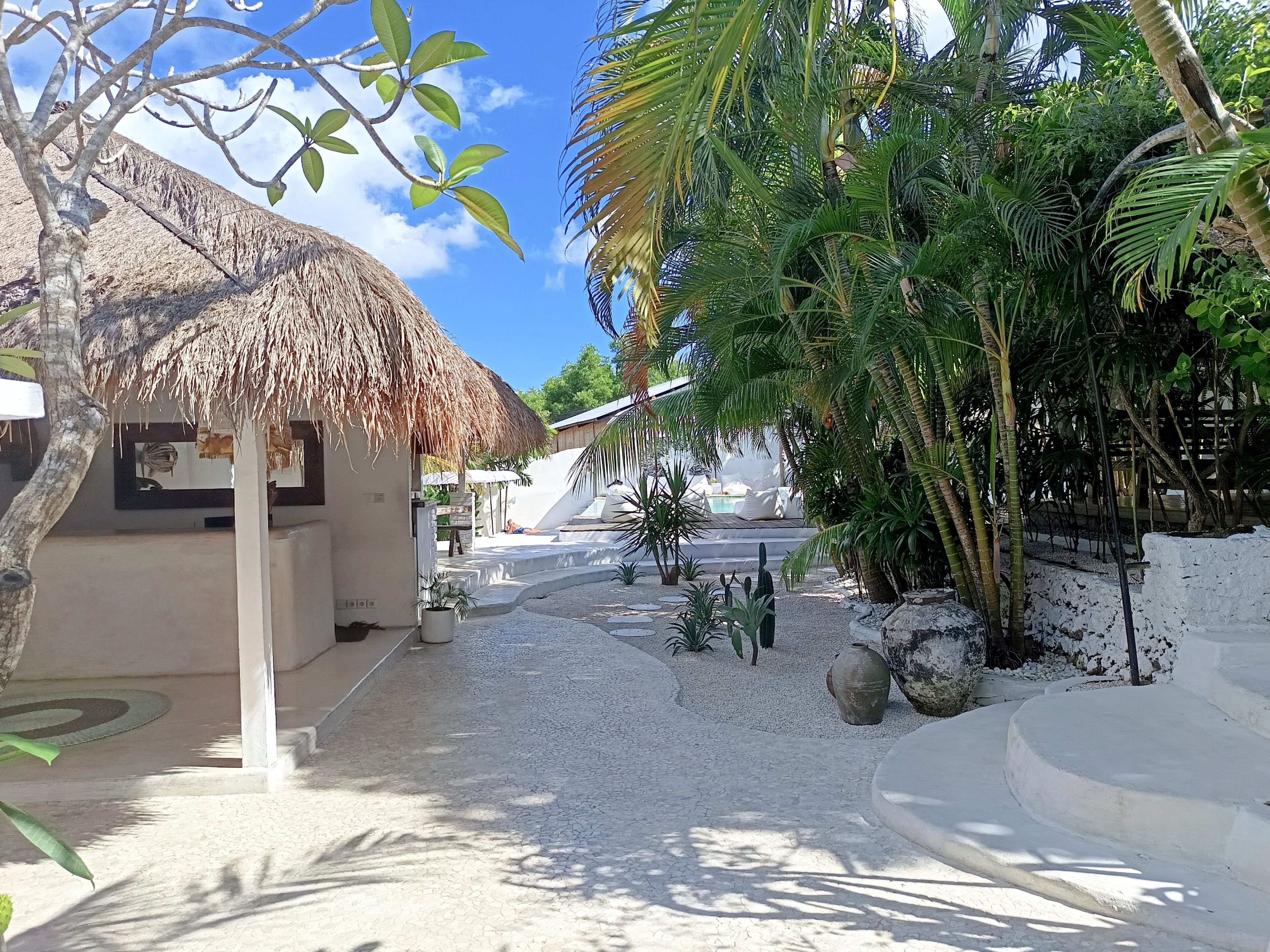 A tropical resort with a thatched-roof structure, palm trees, and a pool area.