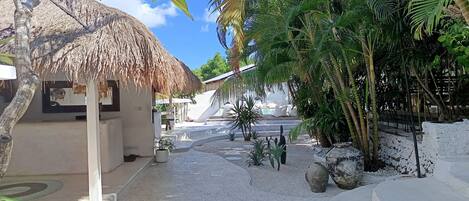 A tropical resort with a thatched-roof structure, palm trees, and a pool area.