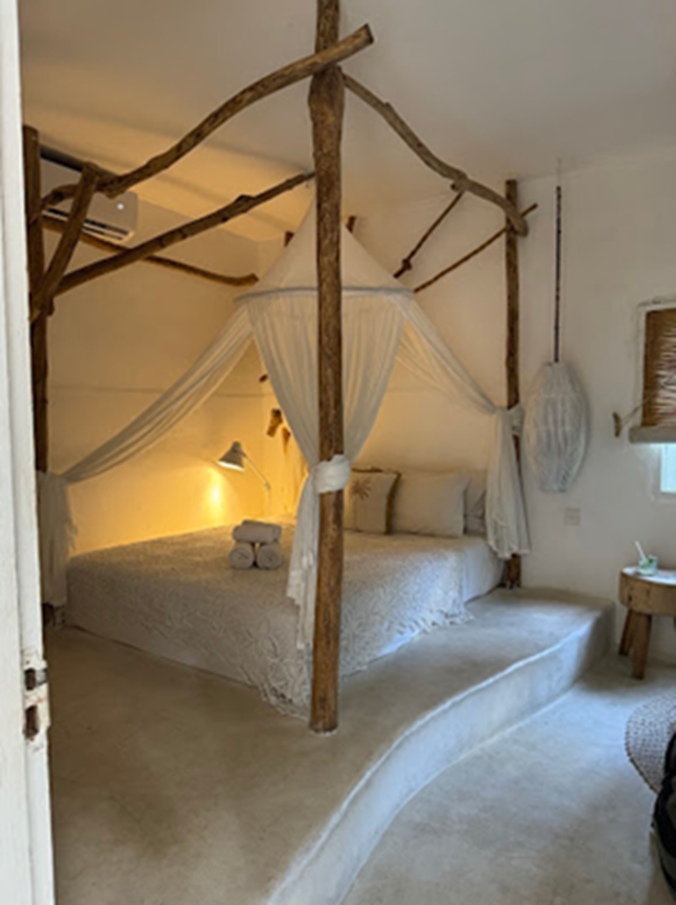 A bedroom with a four-poster canopy bed, a small bedside table, and a lamp.