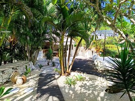 Un sendero en un jardín tropical con palmeras, una terraza de madera y una estructura de techo de paja.