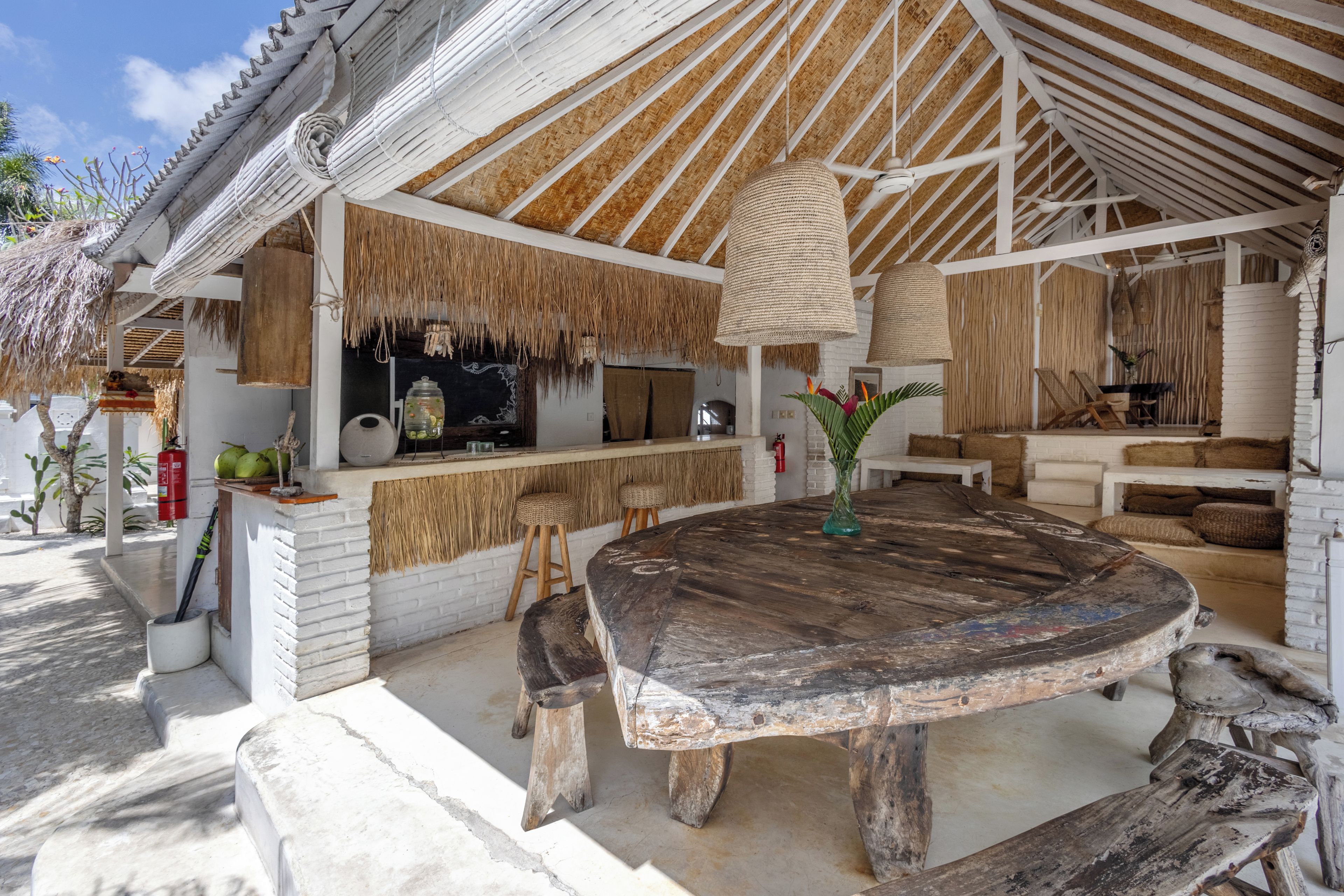 A rustic outdoor dining area with a thatched roof, wooden furniture, and a bar counter.