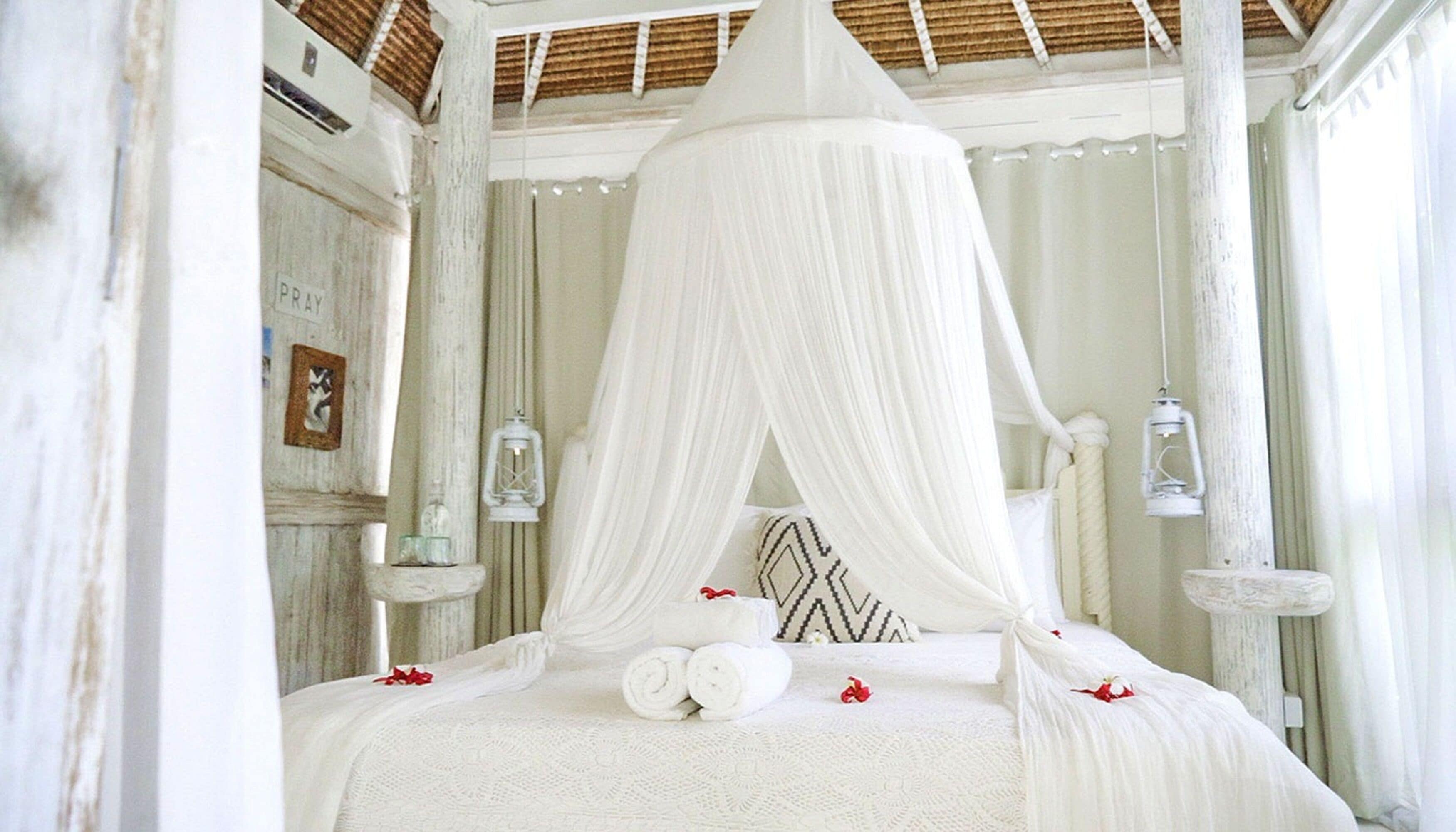 Een wit hemelbed met opgerolde handdoeken en een decoratief kussen.