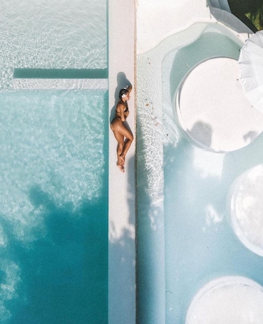 An aerial view of a pool with clear water, a person sitting on the edge, and a circular hot tub area.. Sal Secret Spot