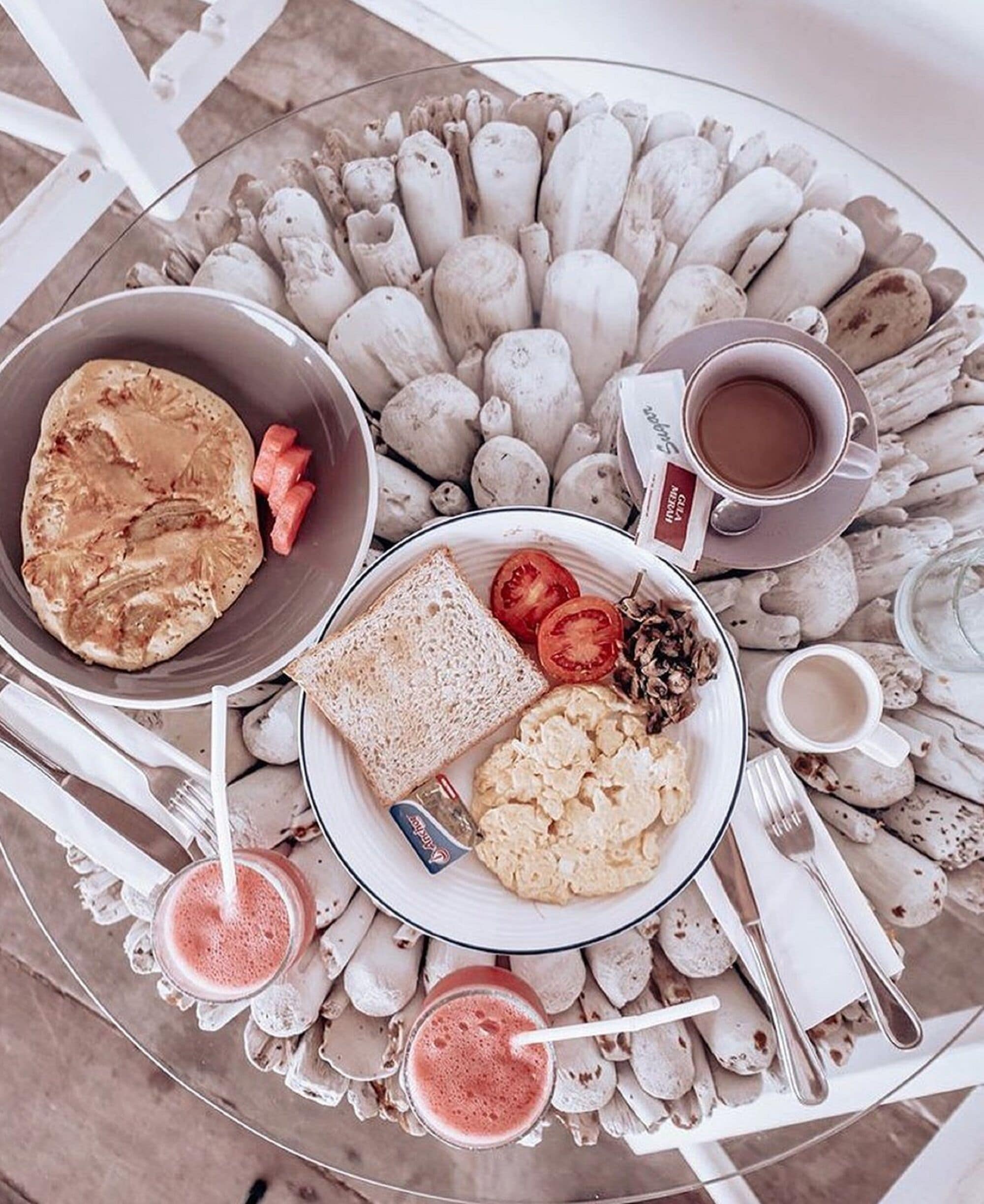 Desayuno con tostadas, huevos revueltos, tomates y una taza de café sobre una mesa rodeada de cáscaras de huevo de cerámica blanca.