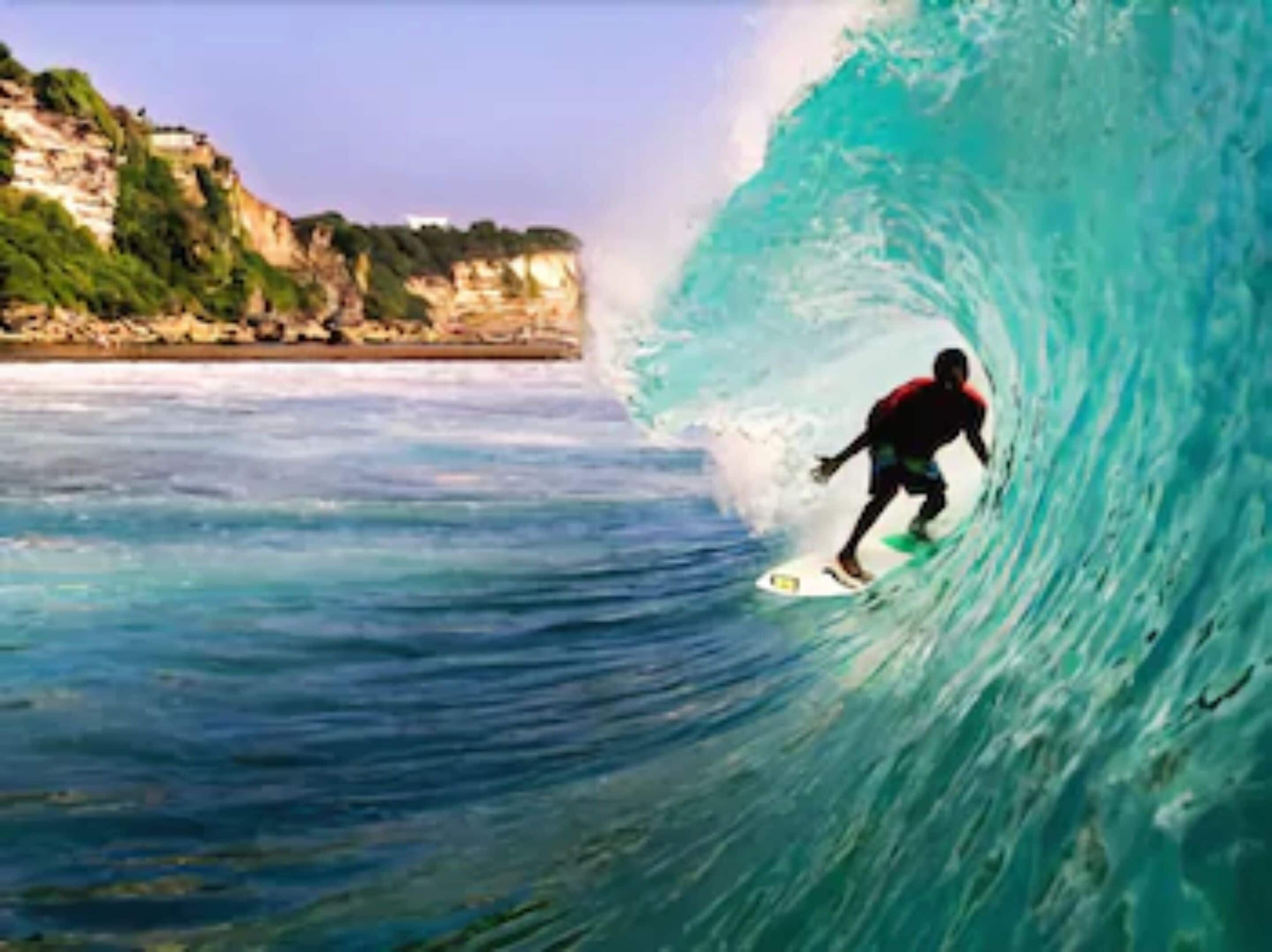 A surfer riding a large wave with a coastal landscape in the background.