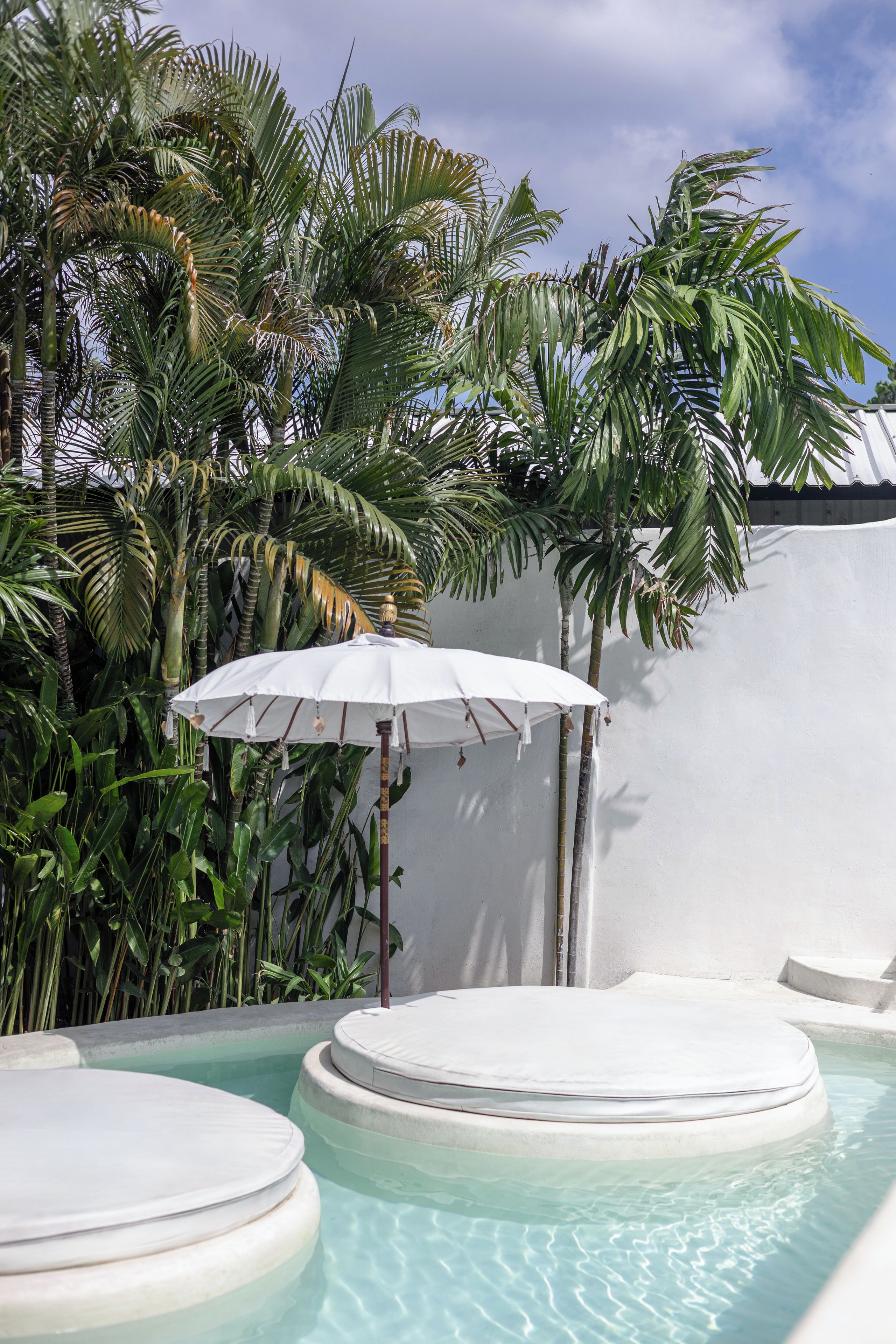 A pool area with a hot tub and an umbrella, surrounded by lush tropical plants.