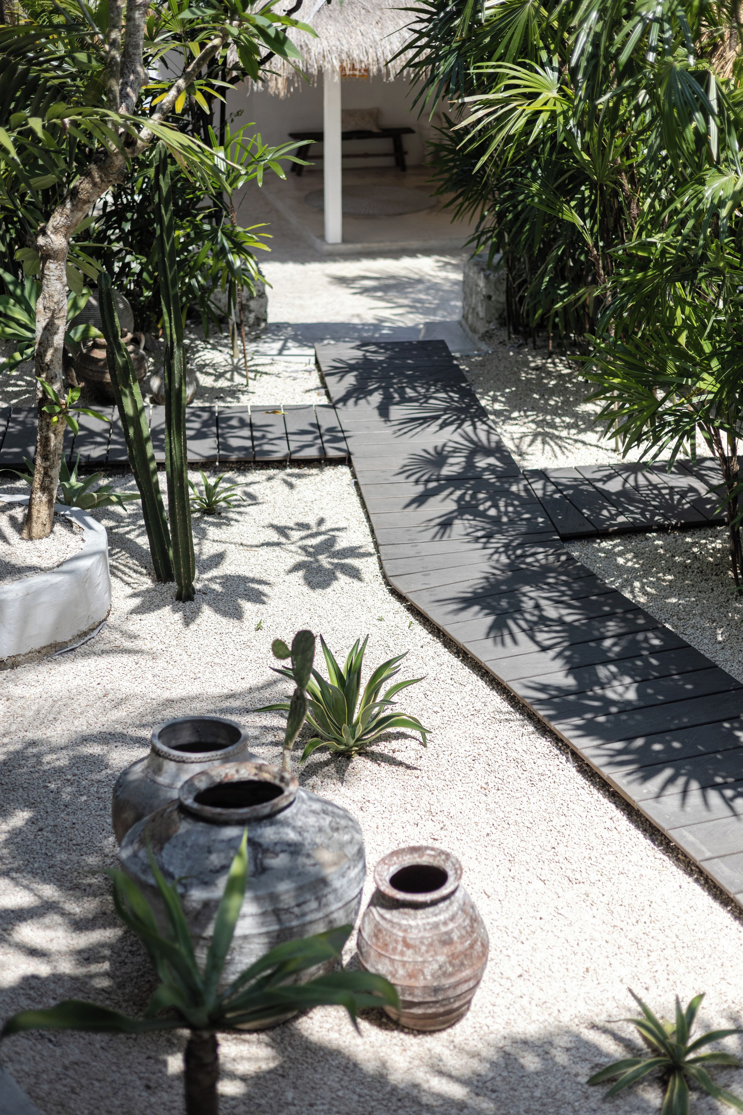 A pathway lined with tropical plants and a thatched-roof structure.