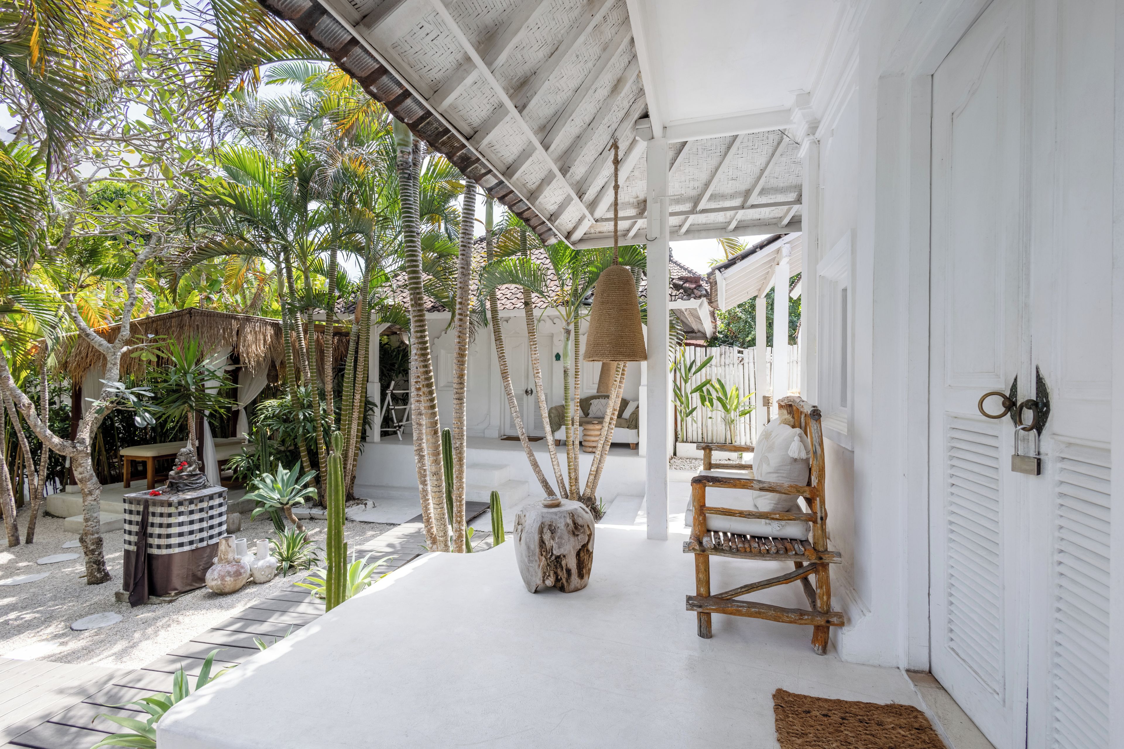 A covered outdoor area with a white building, a wooden bench, and various plants.