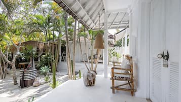 Un espacio al aire libre cubierto con un edificio blanco, un banco de madera y diversas plantas.