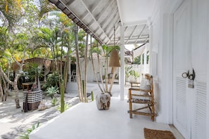 A covered outdoor area with a white building, a wooden bench, and various plants. - Sal Secret Spot (Pecatu)