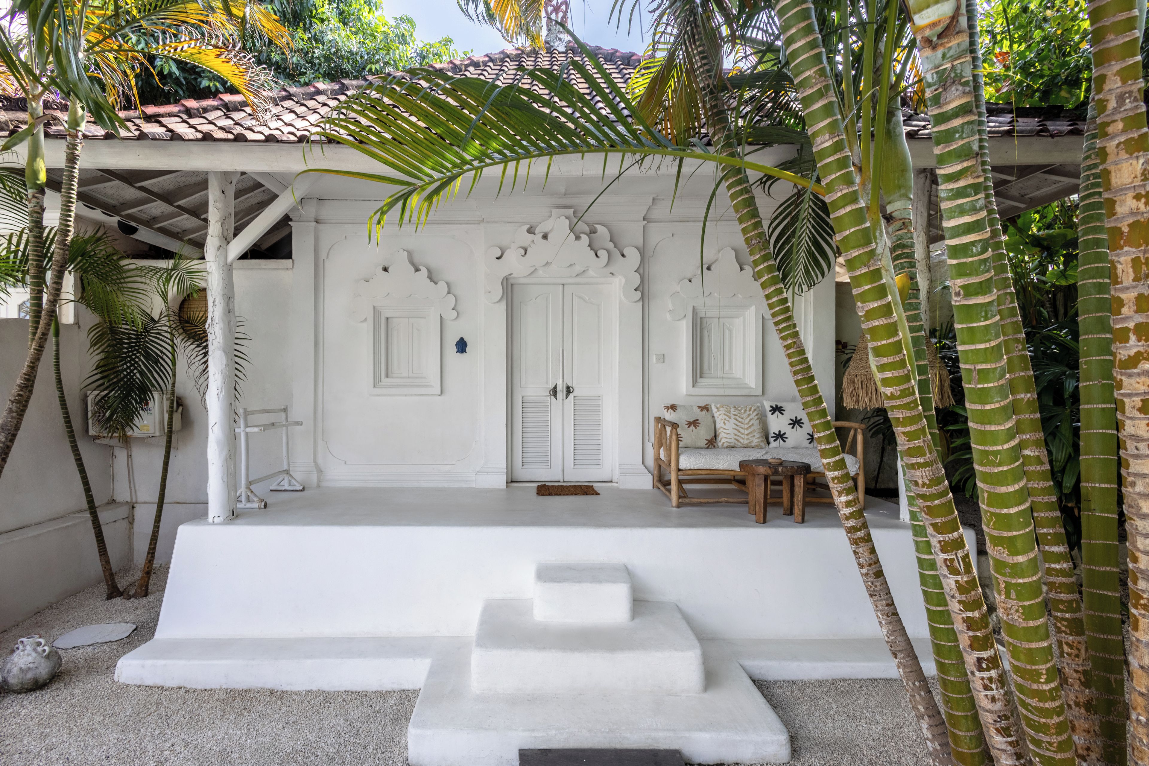 A white building with a tiled roof, two doors, a bench, and a small table.