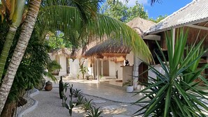 A tropical resort with a thatched-roof structure, palm trees, and a gravel pathway. - Sal Secret Spot (Pecatu)