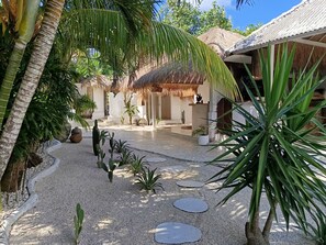 A tropical resort with a thatched-roof structure, palm trees, and a gravel pathway. - Sal Secret Spot (Pecatu)