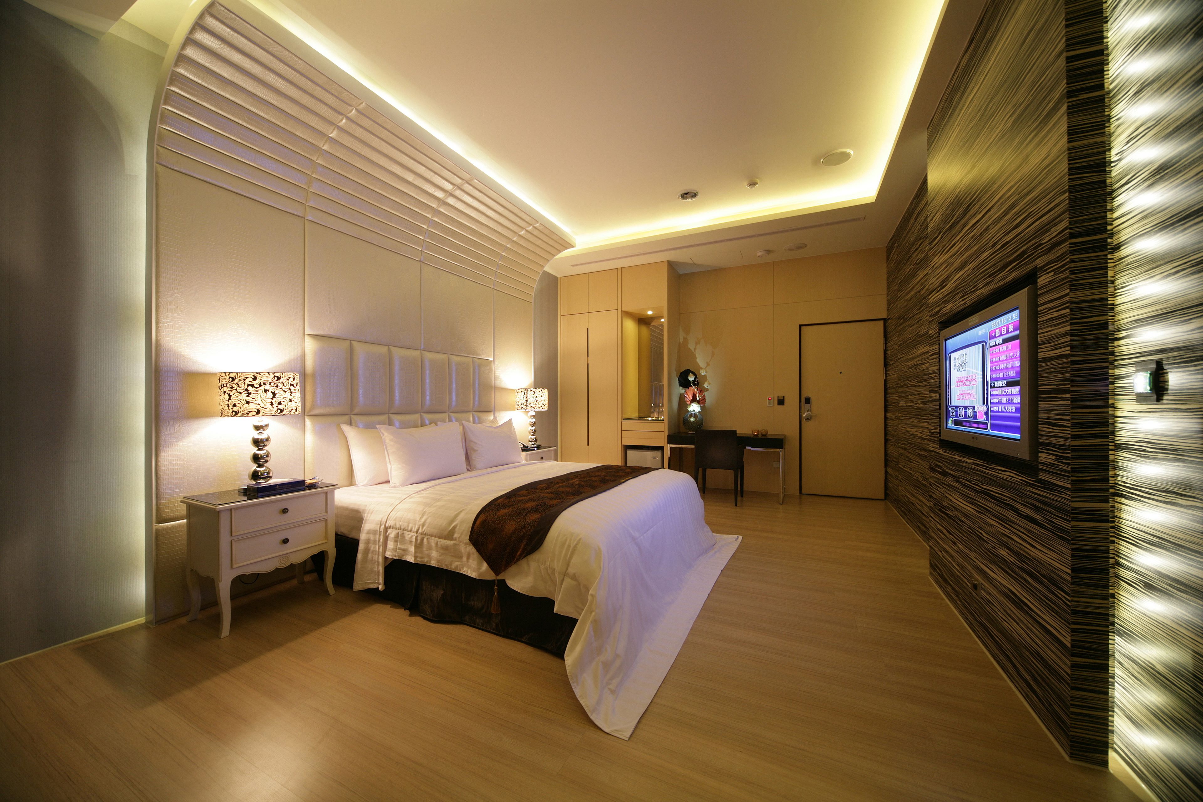 Een moderne hotelkamer met een groot bed, nachtkastjes, een bureau en een aan de muur bevestigde televisie.