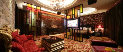 A luxurious hotel room with a red sofa, a large flat-screen TV, a chandelier, and a patterned carpet.