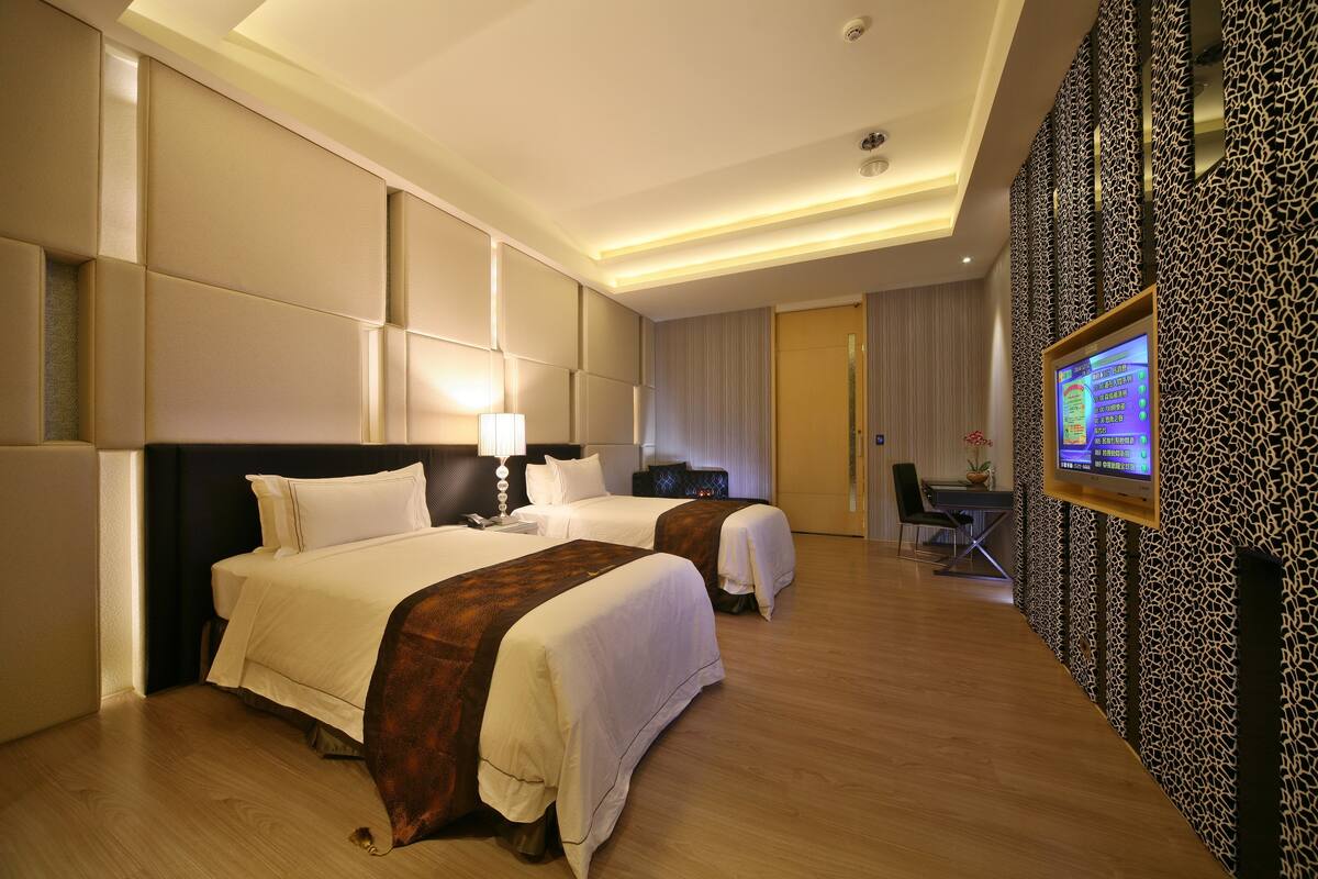 Habitación de hotel con dos camas, un escritorio, una silla, un televisor y un papel tapiz estampado.