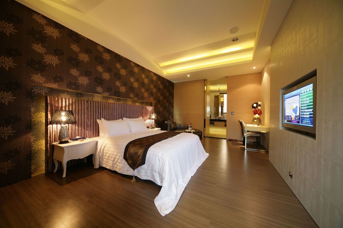A hotel room with a large bed, a desk, a chair, and a television on the wall.