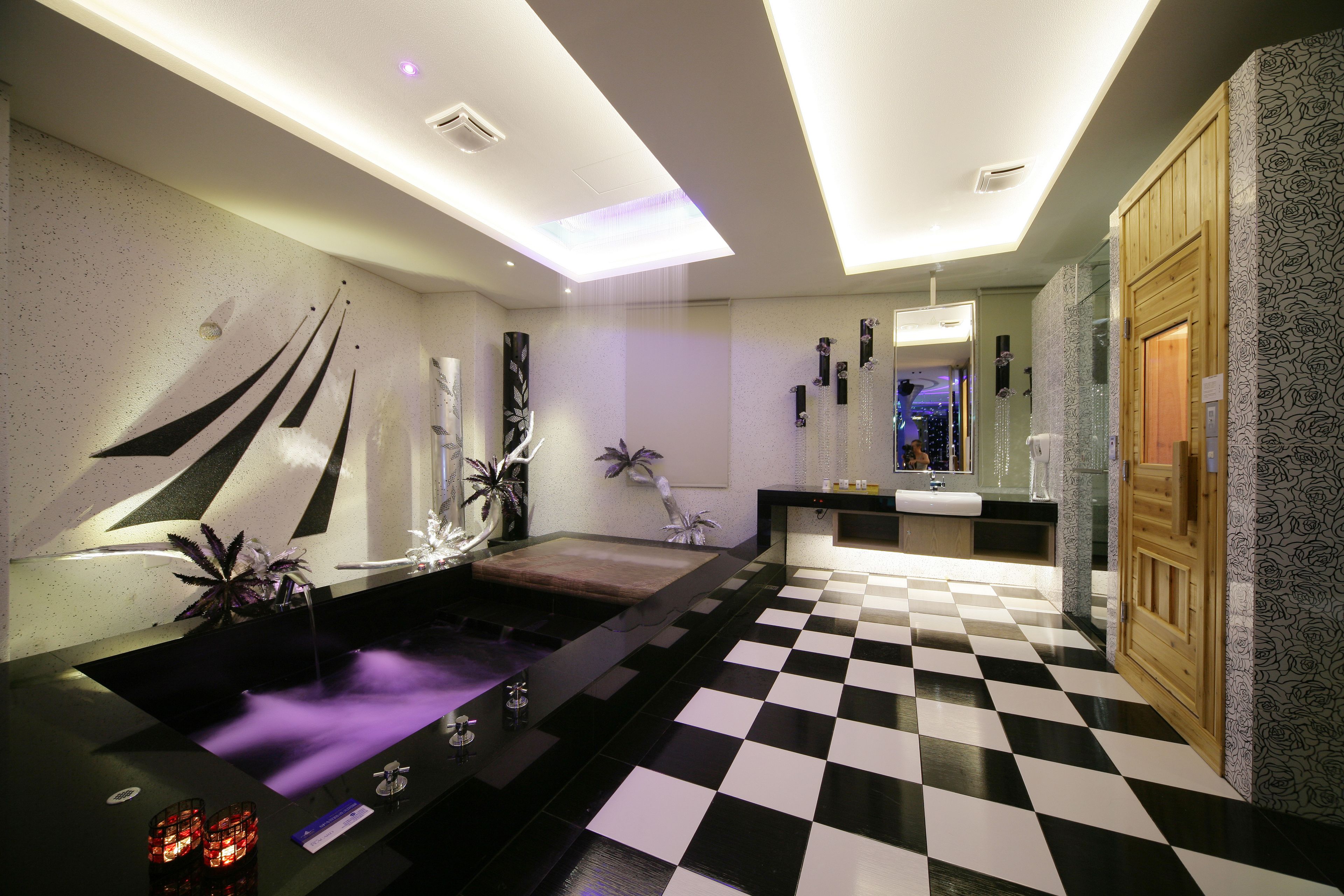 Une salle de bain moderne avec un carrelage à motifs géométriques, un grand miroir et une porte en bois.