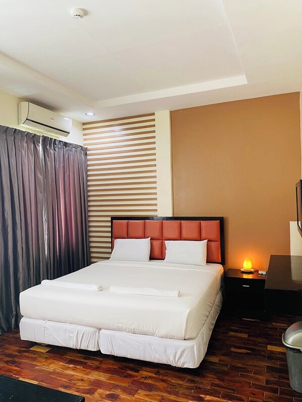 A hotel room with a large bed, a nightstand with a lamp, and a wall-mounted air conditioner. - Arabelle Suites (Tagbilaran)